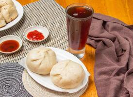 2 Steamed Buns with Dipping Sauces and a tall glass of iced tea isolated on napkin side view of taiwan dim sum food photo
