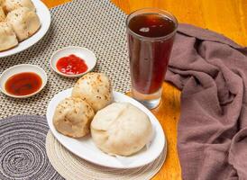 2 pan fried buns and 1 pepper pork bun with Dipping Sauces and a tall glass of iced tea isolated on napkin side view of taiwan dim sum food photo