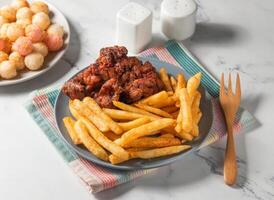 Fried Chicken thighs steak, French fries and potato balls served in plate with fork isolated on napkin side view of taiwan food photo