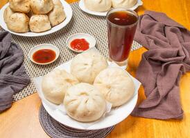 4 steamed pepper meat buns with Dipping Sauces and a tall glass of iced tea isolated on napkin side view of taiwan dim sum food photo