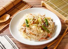 Fried Rice Noodles with Vermicelli, Mushroom and Shredded Pork served in plate with chopsticks and spoon isolated on wooden table side view of taiwan food photo
