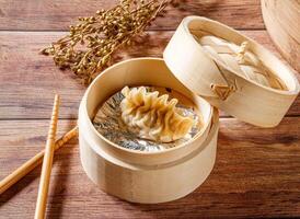 Steamed Sharks fin dumplings in Bamboo Steamer with chopsticks isolated on wooden table side view of dim sum taiwan food photo