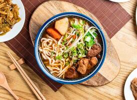 Vegetarian Beef Noodle Soup topped with green onion and coriander served in bowl with chopsticks and spoon isolated on wooden board top view of taiwan food photo