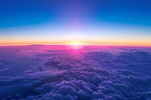 A stunning aerial view of a vibrant sunset above the clouds, captured from an airplane window. The sky is painted with warm hues of orange, pink, and purple, creating a serene photo