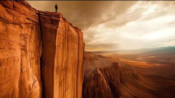Silhouette of a man standing on the edge of a high cliff, surrounded by a stunning desert landscape. A display of nature's magnificence, vastness, and a sense of freedom. photo