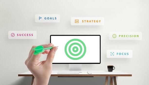 Hand holding a dart aiming at a target displayed on a desktop monitor, surrounded by words like goals, strategy, and success, symbolizing the integration of technology, marketing, and precision photo
