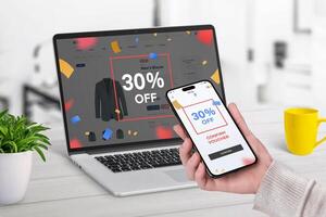 Girl uses her smartphone to confirm a 30 off voucher received as a reward via a pop-up on an eCommerce website viewed on her laptop photo