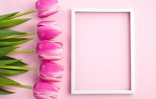 Flat lay with beautiful bouquet of pink tulips and white vertical frame on pink background. Close-up. Top view. Copy space. photo