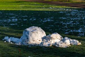 In a park, remnants of snow lay on the green grass, contrasting with photo