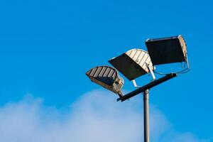 Three evenly spaced light fixtures are mounted on a tall pole against photo