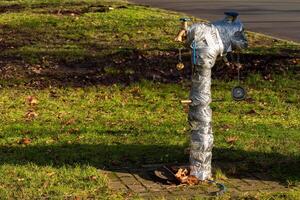 A fire hydrant wrapped in grey tape stands on a grassy area in a park photo