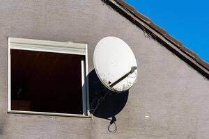 Satellite dish mounted outside a window on a gray building photo