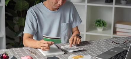 Elderly man calculating savings with a calculator and notebook at home photo