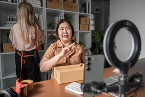 E-commerce entrepreneur explaining shipment process on camera with package, while assistant organizes inventory photo