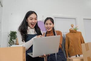 Excited online sellers celebrating success while reviewing orders on a laptop in a cozy clothing store photo