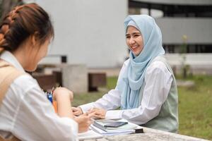 Female student in hijab smiling while studying with a friend outdoors. photo