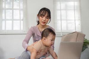 Focused mother assisting her baby while working on a laptop at home. photo