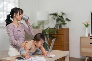 Mother sipping coffee while supervising her baby exploring a desk. photo