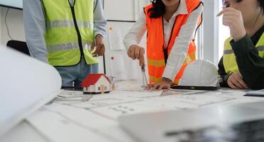 Construction team analyzing blueprints with a house model and measuring tool in a collaborative office environment photo