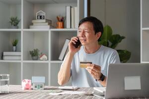 Smiling man using smartphone and credit card for online shopping while talking on the phone photo