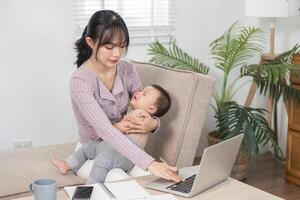 Working mother multitasking with baby on her lap while managing tasks from home office photo
