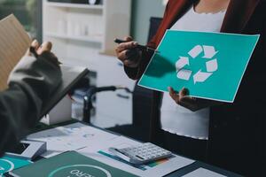 A woman holding a recycling sign in front of a desk photo
