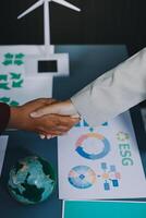 Two people shaking hands over a table with a globe and wind turbines photo