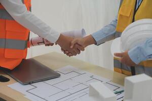 Two people shaking hands over a table with construction plans photo