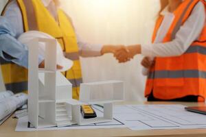 Two people shaking hands over a table with construction plans photo