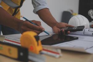 A man in a hard hat and safety vest is using a calculator and measuring tape photo