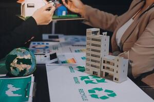 Two people are working on a project with a model of a house and recycling photo