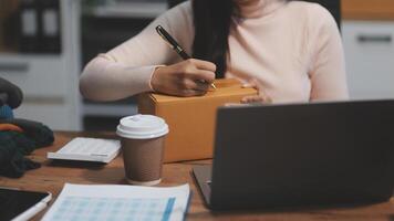 A woman is writing on a piece of paper while sitting at a desk with a laptop and a photo