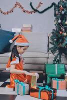 A little girl in a santa hat sitting on the floor with presents photo