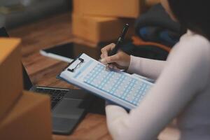 A woman writing on a clipboard while sitting at a desk with boxes and a laptop photo
