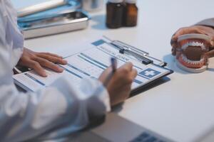 A doctor is writing on a clipboard with a tooth model photo
