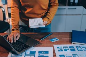 A person is using a laptop and a calculator on a desk photo
