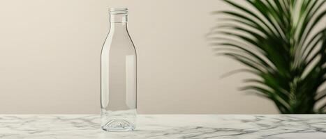 Future lifestyle minimal concept. Empty glass bottle on a marble surface with a plant in the background. photo