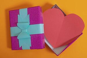parte superior ver de un abierto regalo caja con un rojo corazón en un vibrante naranja antecedentes para San Valentín día y de la madre día. foto