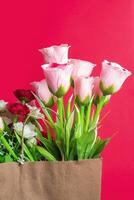 Beautiful bouquet of artificial flowers in a brown paper bag on a red background photo