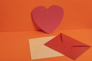 Red paper heart with envelopes on a vibrant orange background for Valentine's Day and Mother's Day. photo