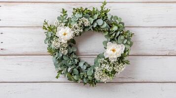 Elegant floral wreath decorated with white flowers and greenery on rustic wooden background photo