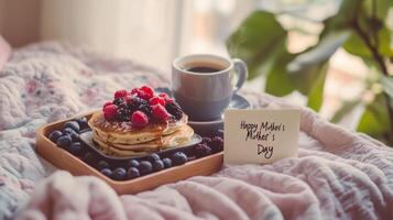 Breakfast tray with pancakes, berries, coffee, and a greeting card celebrating Mother's Day in a cozy indoor setting photo
