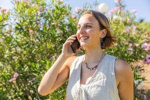 A woman is talking on her cell phone while walking in a park and smiling during a summer day photo