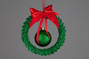 Green Christmas tree toy in the form of a garland with a ball and a red bow on a gray background. photo