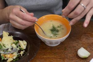 A plate of soup sprinkled with herbs and a hand with a spoon. Simple lunch at home. photo