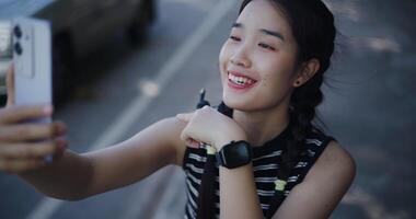 Handheld high angle view shot, Cheerful Asian woman sits on an outdoor sidewalk and enjoys a fun call with her friends via smartphone video