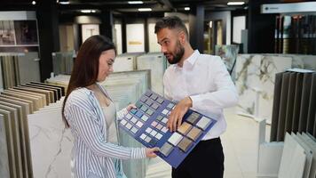 A salesman assists a female customer in selecting tiles, showing her various color and texture options in the showroom to help find the perfect match video