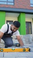 un construcción trabajador usos un nivel herramienta a precisamente alinear pavimentación piedras durante instalación video