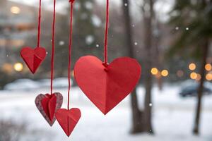 Red paper hearts, crafted and strung with twine, dangle from a window in a snowy winter scene. photo