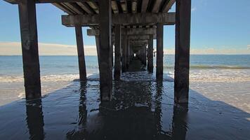 Underneath ocean pier with calm water reflections, View under a pier with ocean waves reflecting the structure above. video